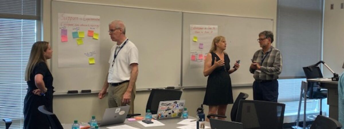 4 researchers standing in front of white board engaged in conversation.