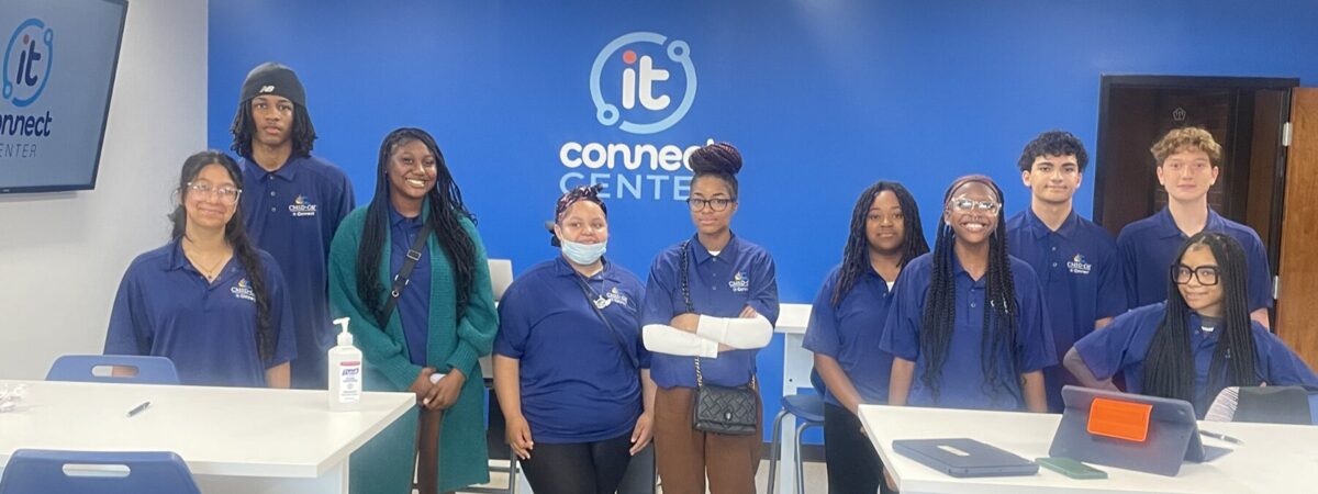 Students wearing their blue student tech team shirts posing in front of the IT Connect Center logo