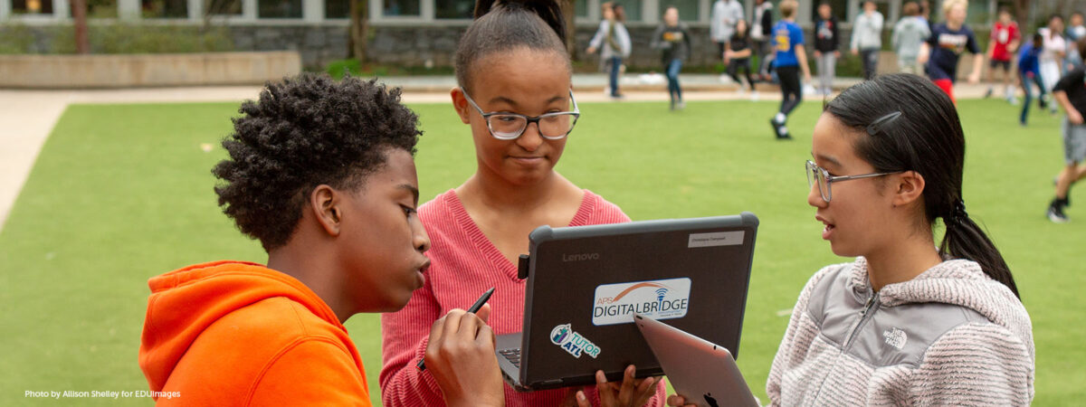 Three eighth-grade students work together on an assignment in a school courtyard.