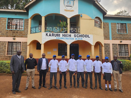 A group of students and their teachers stand together in front of their high school.