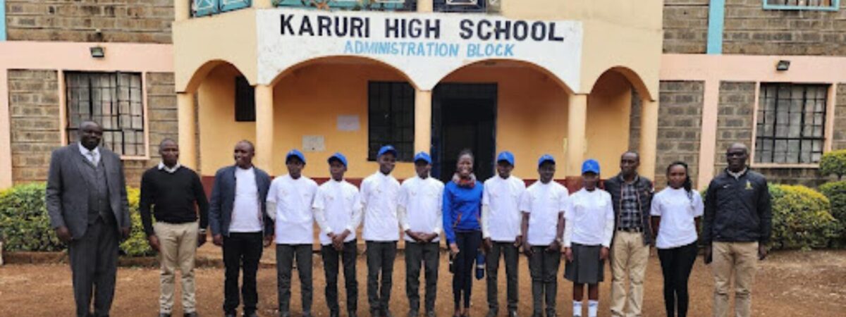 A group of students and their teachers stand together in front of their high school.