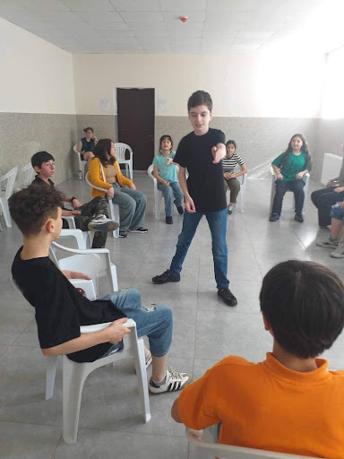 Students site in a circle while one student speaks to the group from the center of the circle. 