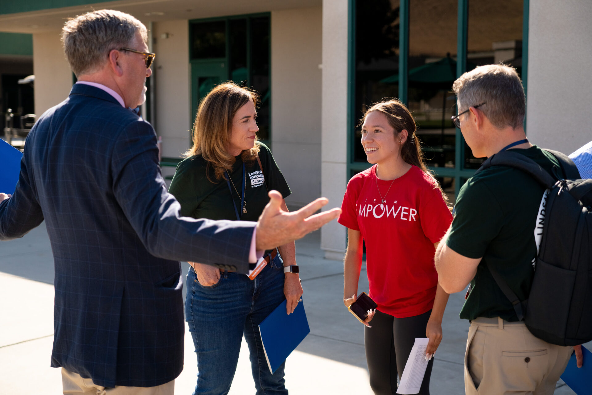 Image of 3 adults (2 white males and 1 Latina female) speak with a teenage student outdoors 