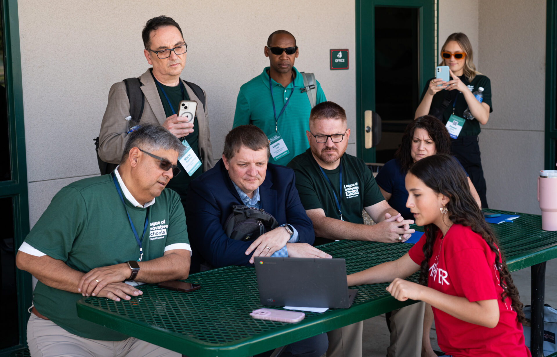 Adults sit at a table with a teenage student who shows something to them on her laptop. 