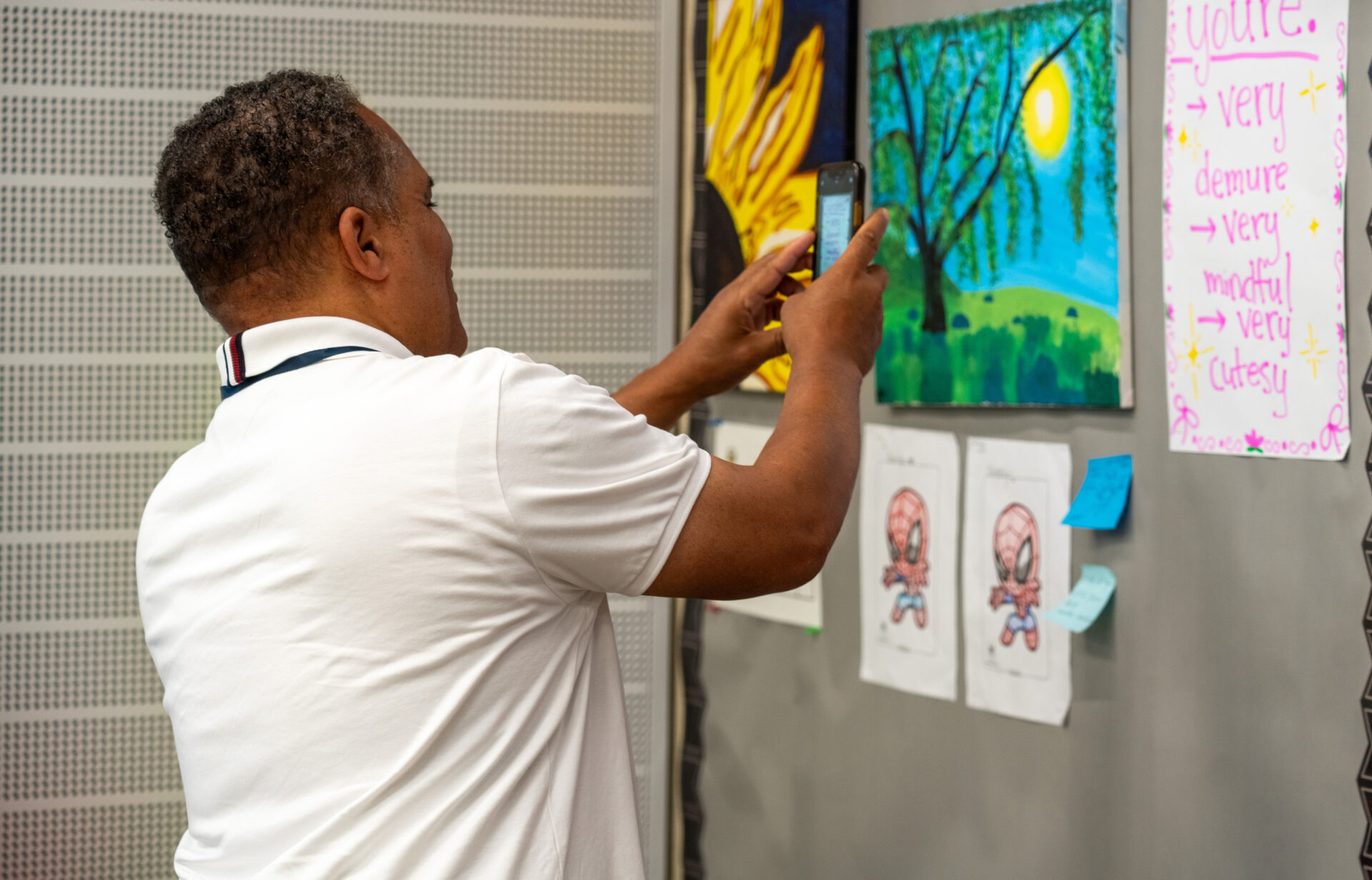 A black male adult takes a photo of a bulletin board with his phone. 