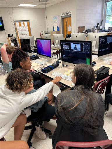 Students huddle together in front of a computer screen.