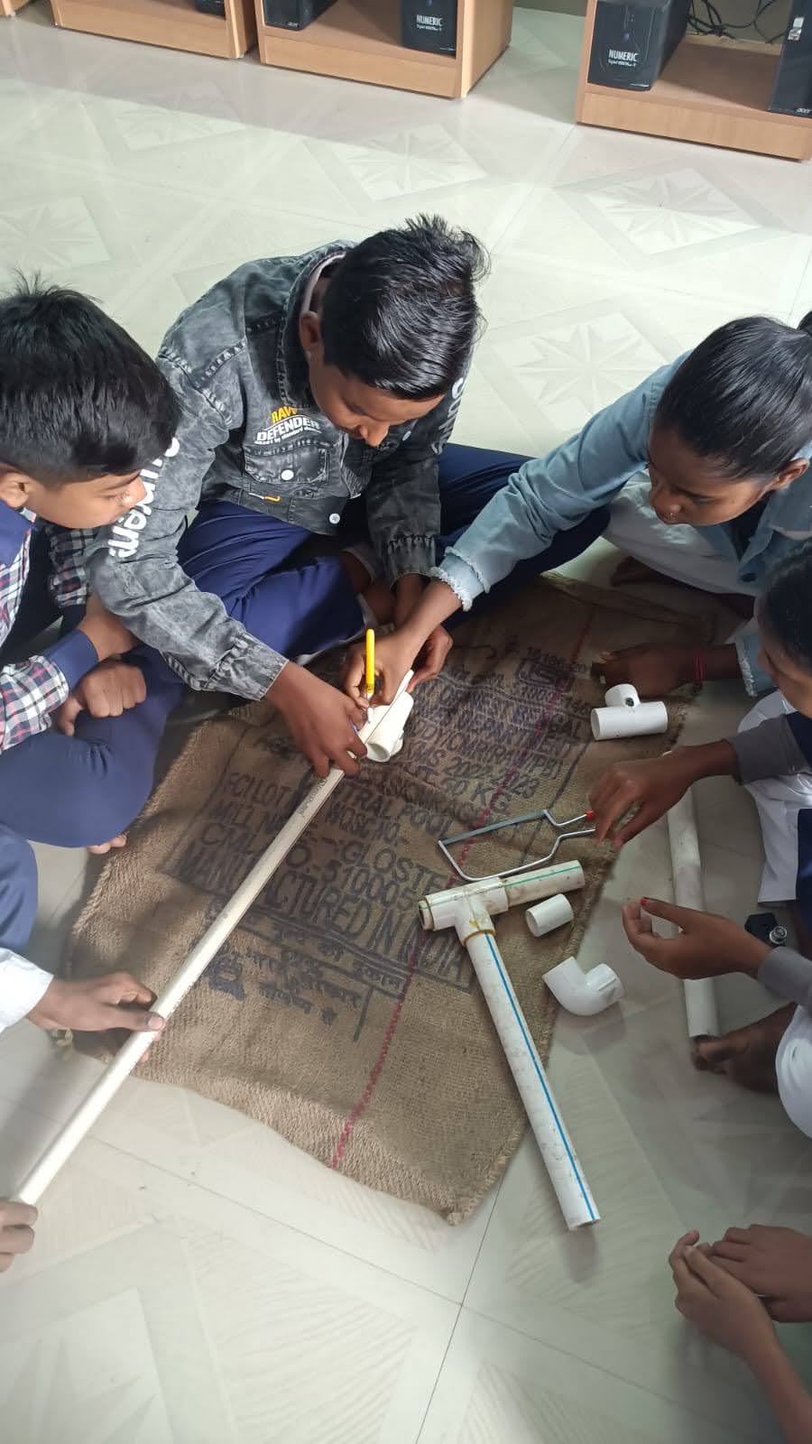 A group of students sit together on the floor to measure materials. 