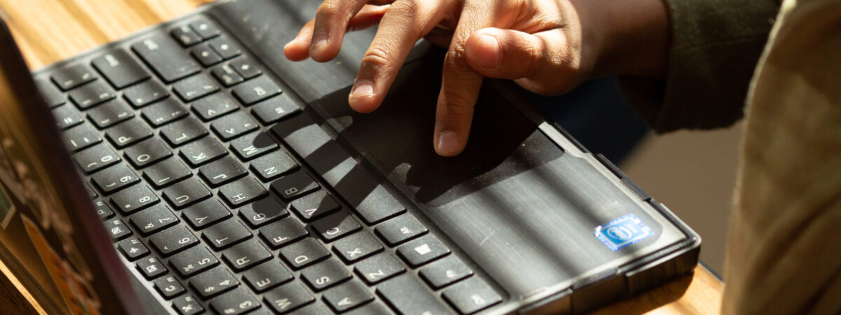 A close-up view of hands typing on a black laptop keyboard, with sunlight casting shadows across the keys.