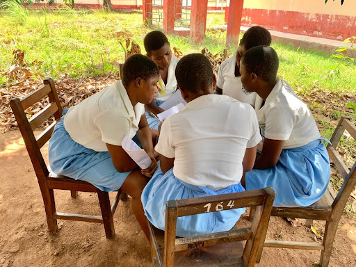 Five students huddle over a sheet of paper with their findings. 