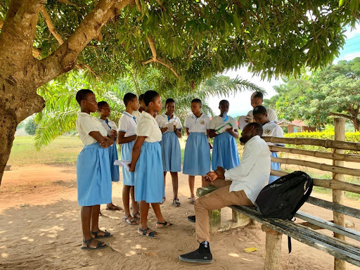 A group of students speak to a man sitting on a bench.