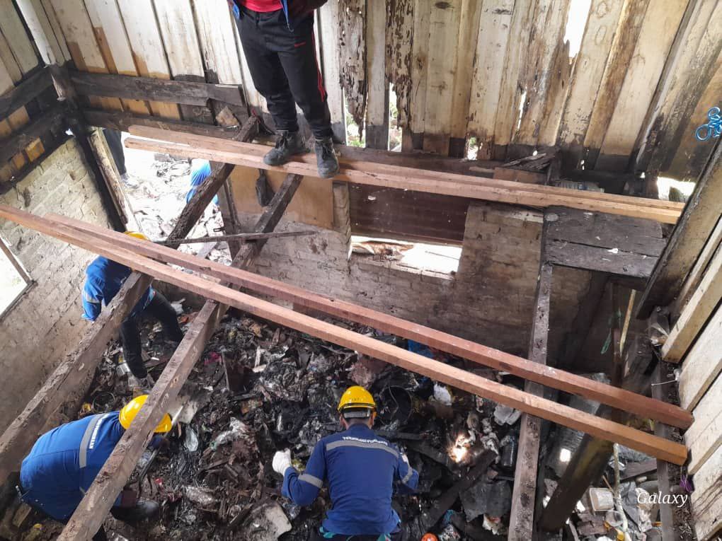 Students work to clear trash underneath wooden beams of the floor. 