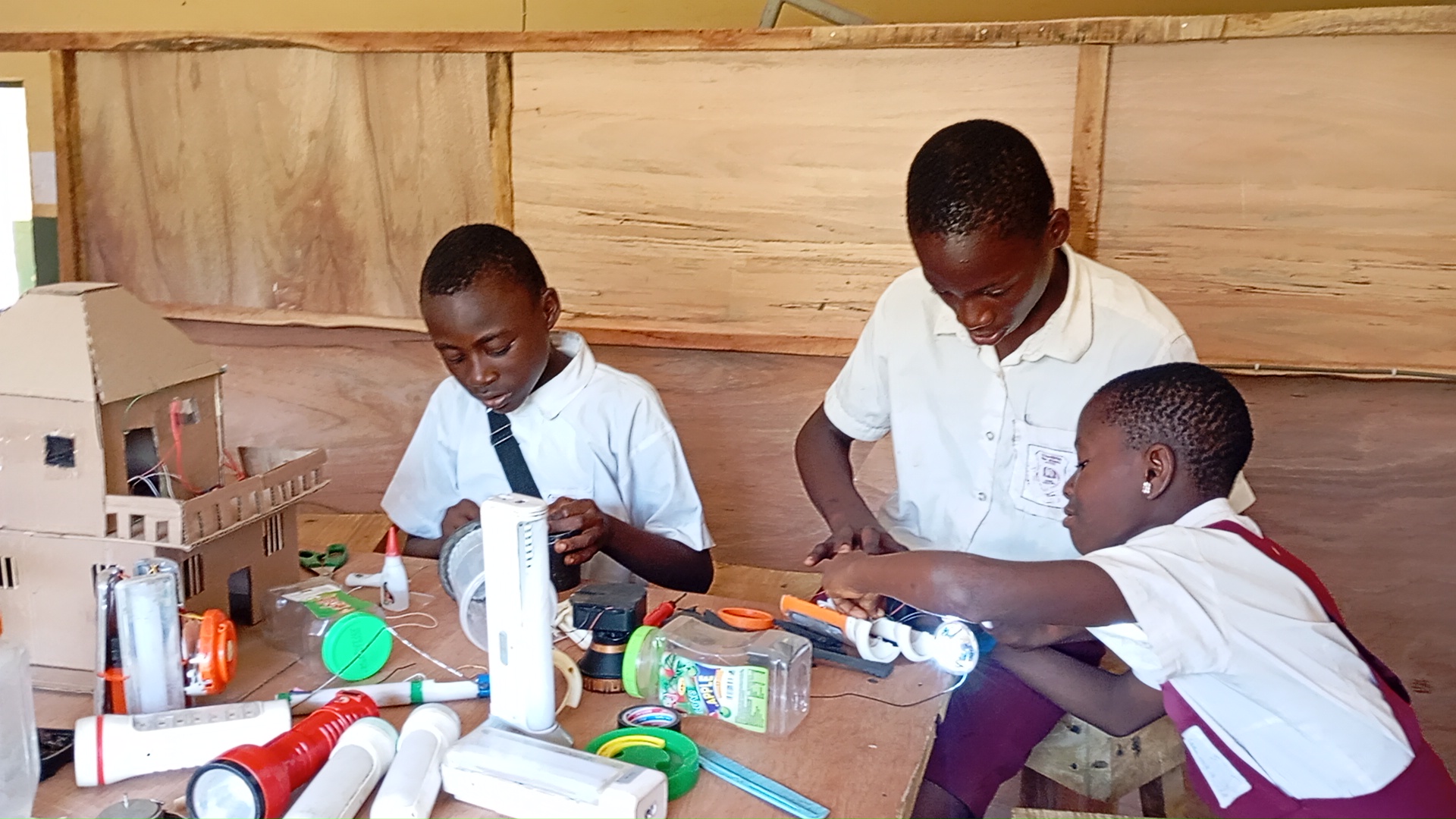 Three students work on small electronic devices at a workstation. 