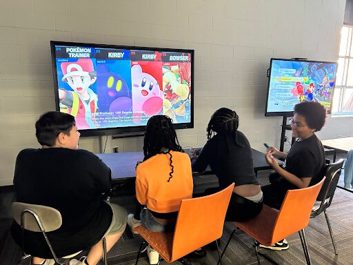 Four students sit in front of a television showing four video game characters. 