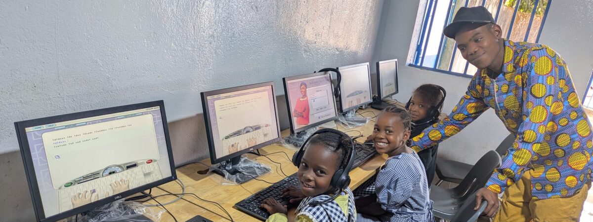 2 students sit at computers and 1 teacher assists them