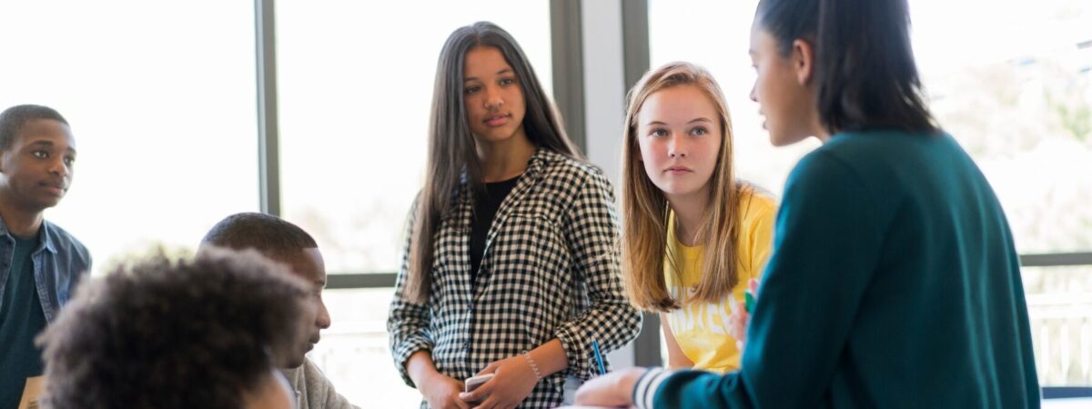 An image of high school aged students sitting in a circle having a discussion.