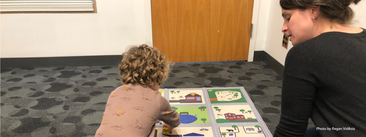 Woman watches over preschooler interacting with a map.
