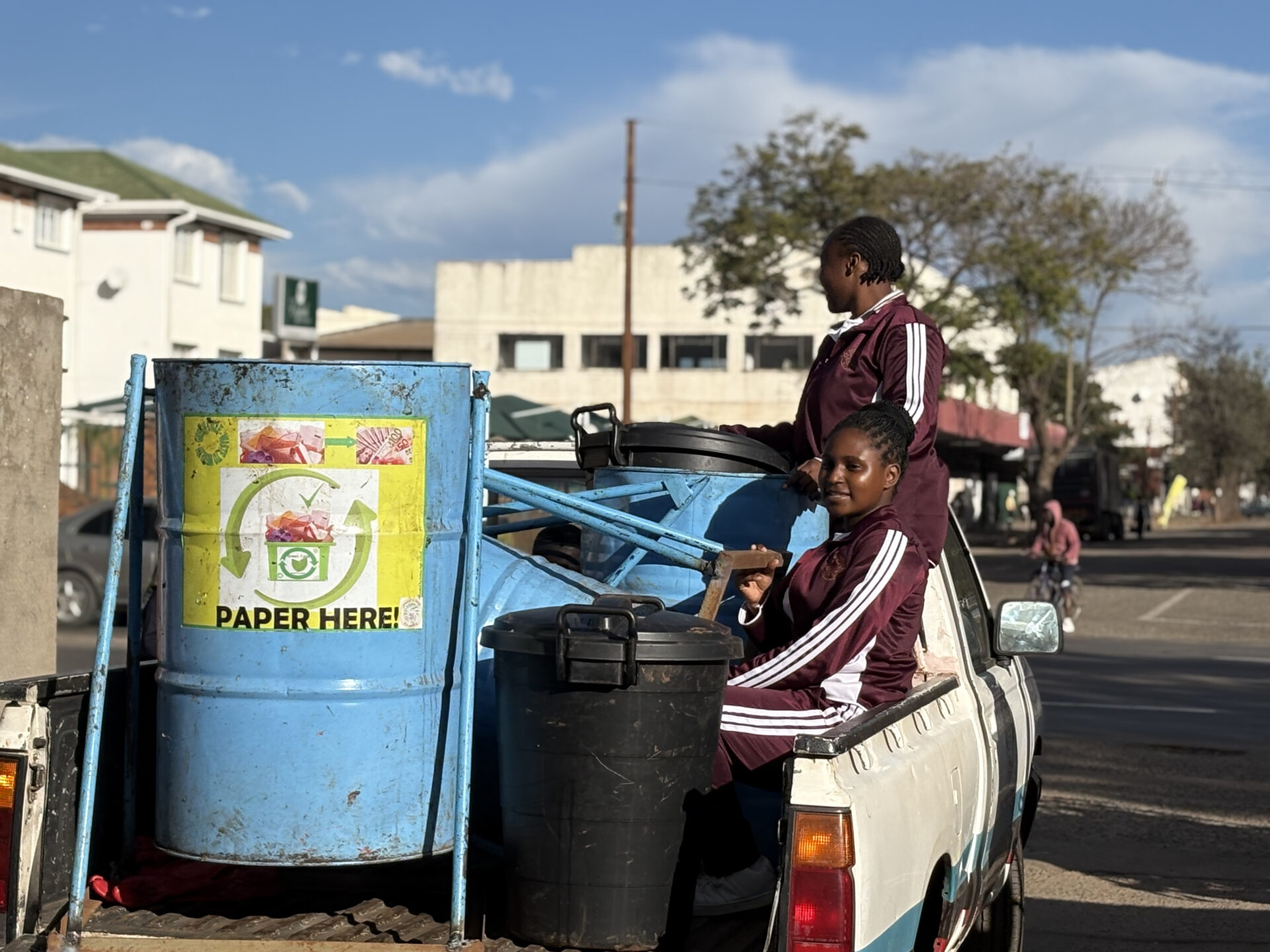 A pick-up truck holds one bin that says “paper here!” and two students in the bed of the truck. 