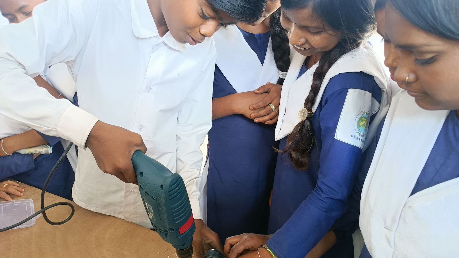 A student uses a power drill while classmates watch.