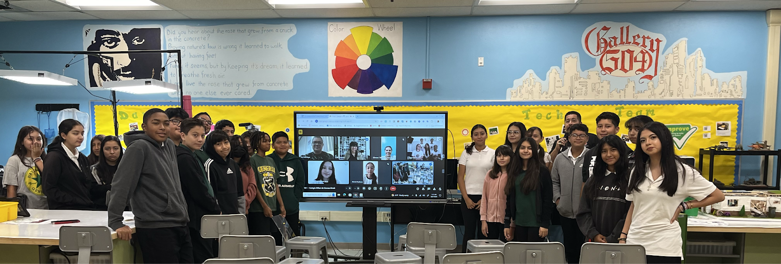 Students gathered around a large screen displaying a Zoom call with peers.