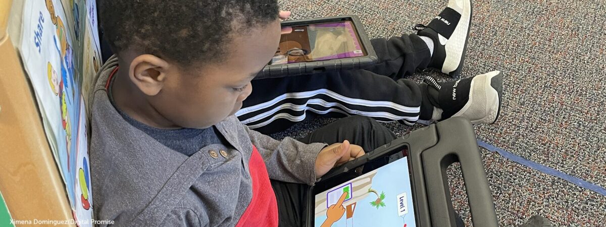 Elementary school student sitting on the floor looking at a tablet device.