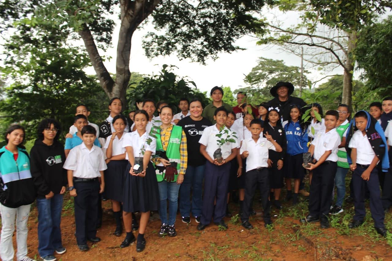 A group of students outdoors, holding potted tree saplings for planting.