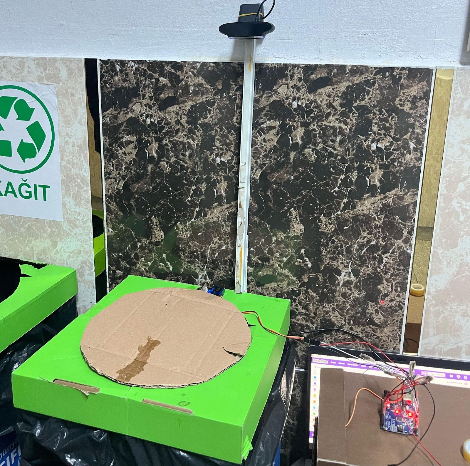 A prototype of a waste bin made from cardboard, with a basic webcam mounted on top and a small sensor attached.