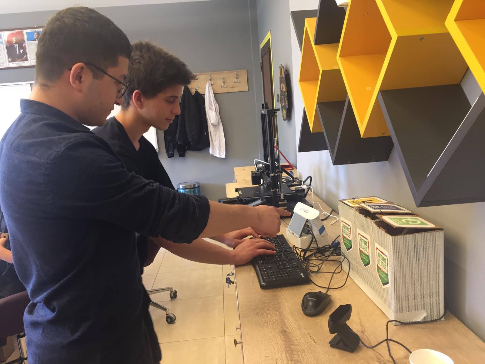 Two students standing in front of a keyboard and cables while looking and pointing at a small sensor.