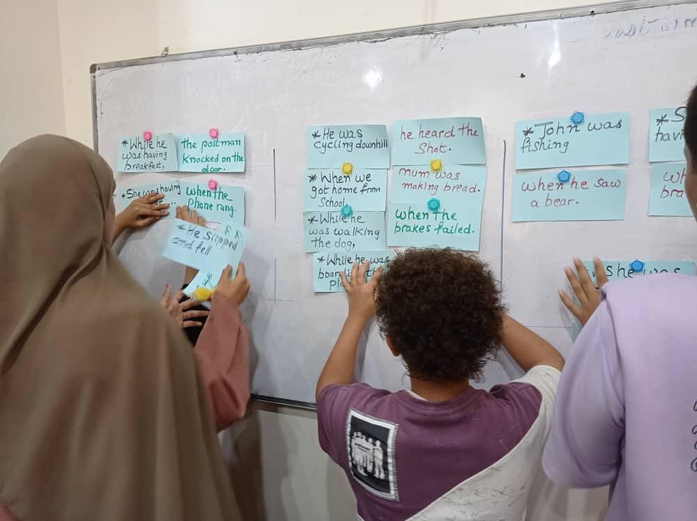 A teacher and students post large post-its on a white board