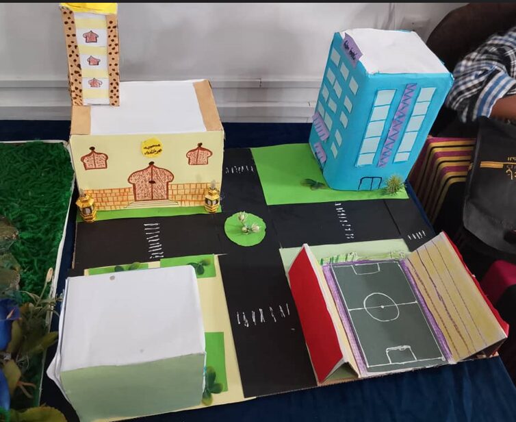 Four mini-building structures made of paper and cardboard sit on a table