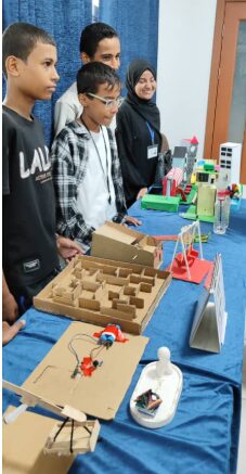 Students stand behind a table holding their cardboard prototypes