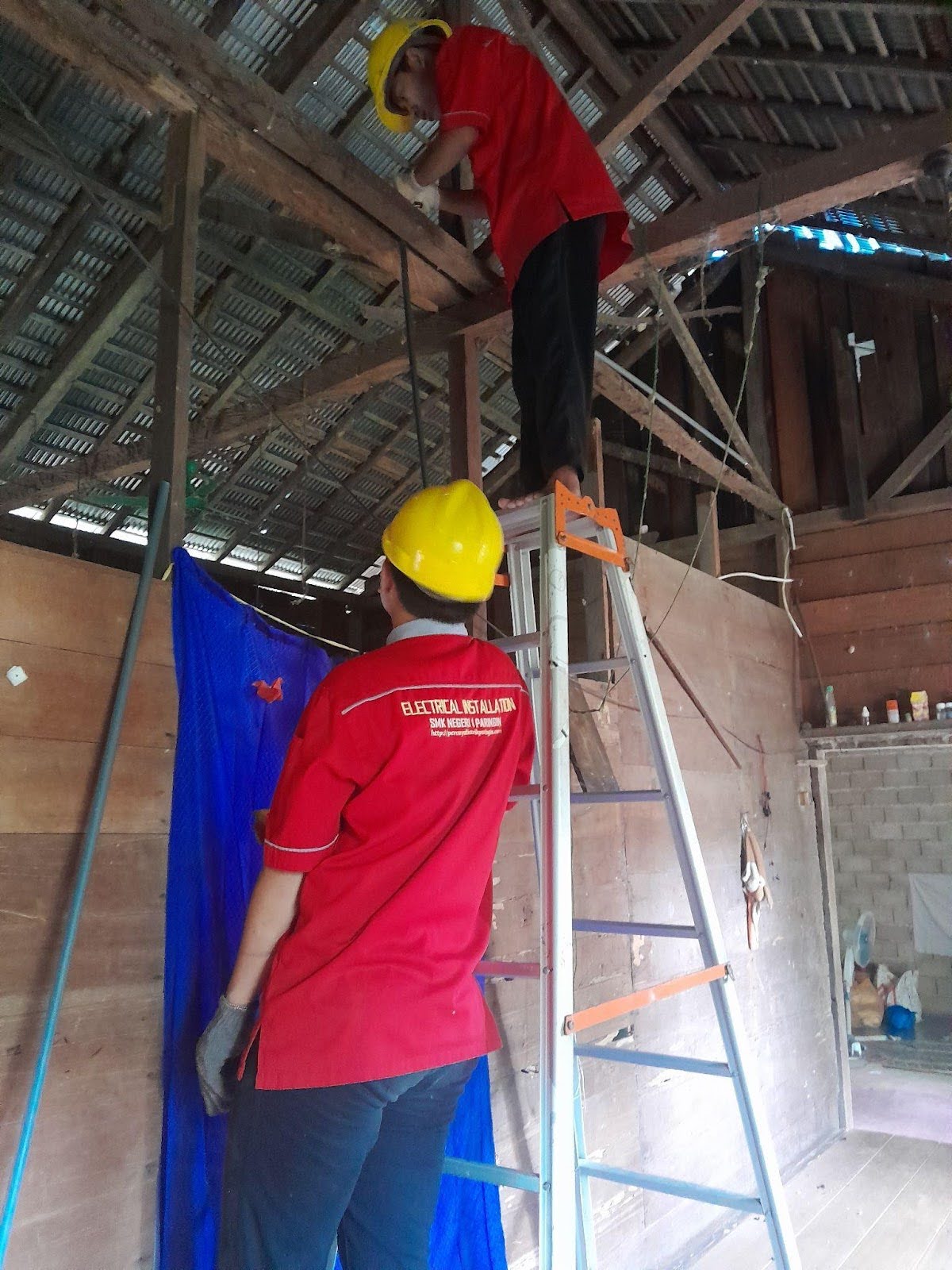 One student is mounted on a ladder and another stands next to the ladder while working on a home repair.