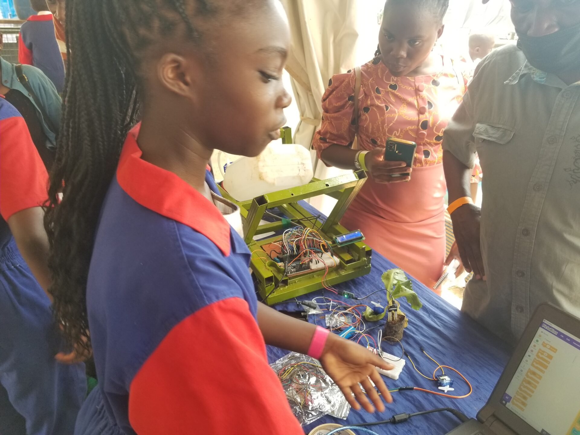 A student stands behind a table presenting her projects while adults listen