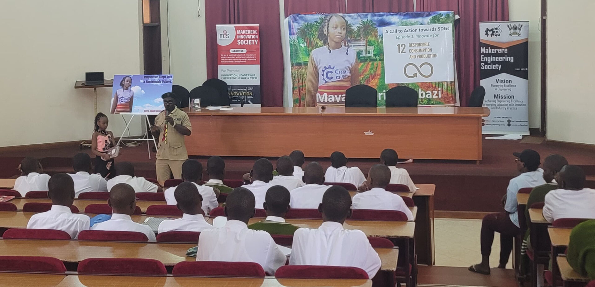 An assembly of students listen to Maya and her teacher speak.