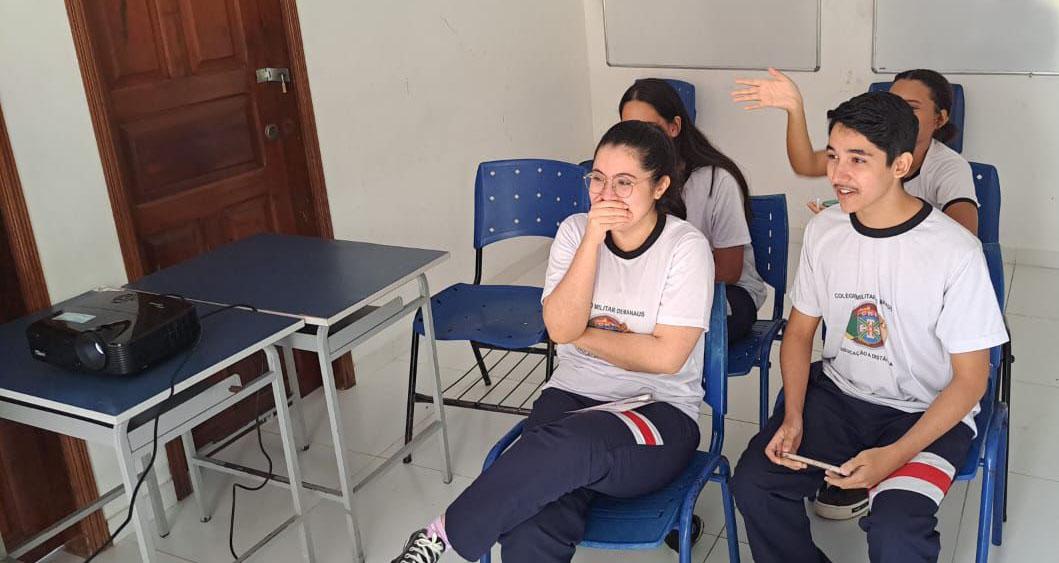 Four students are seated and smiling at a screen that is off-camera