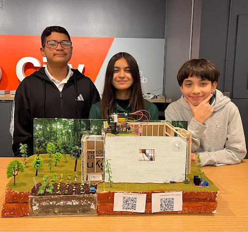 Students smile behind their diorama featuring a house and garden.