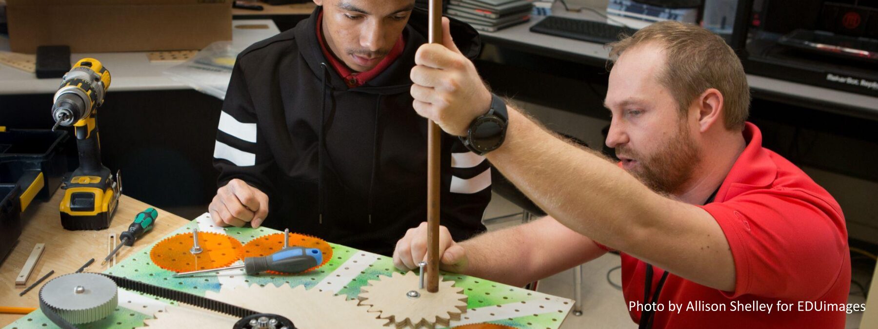 An image of a teacher helping a student mount a pipe on an engineering project.