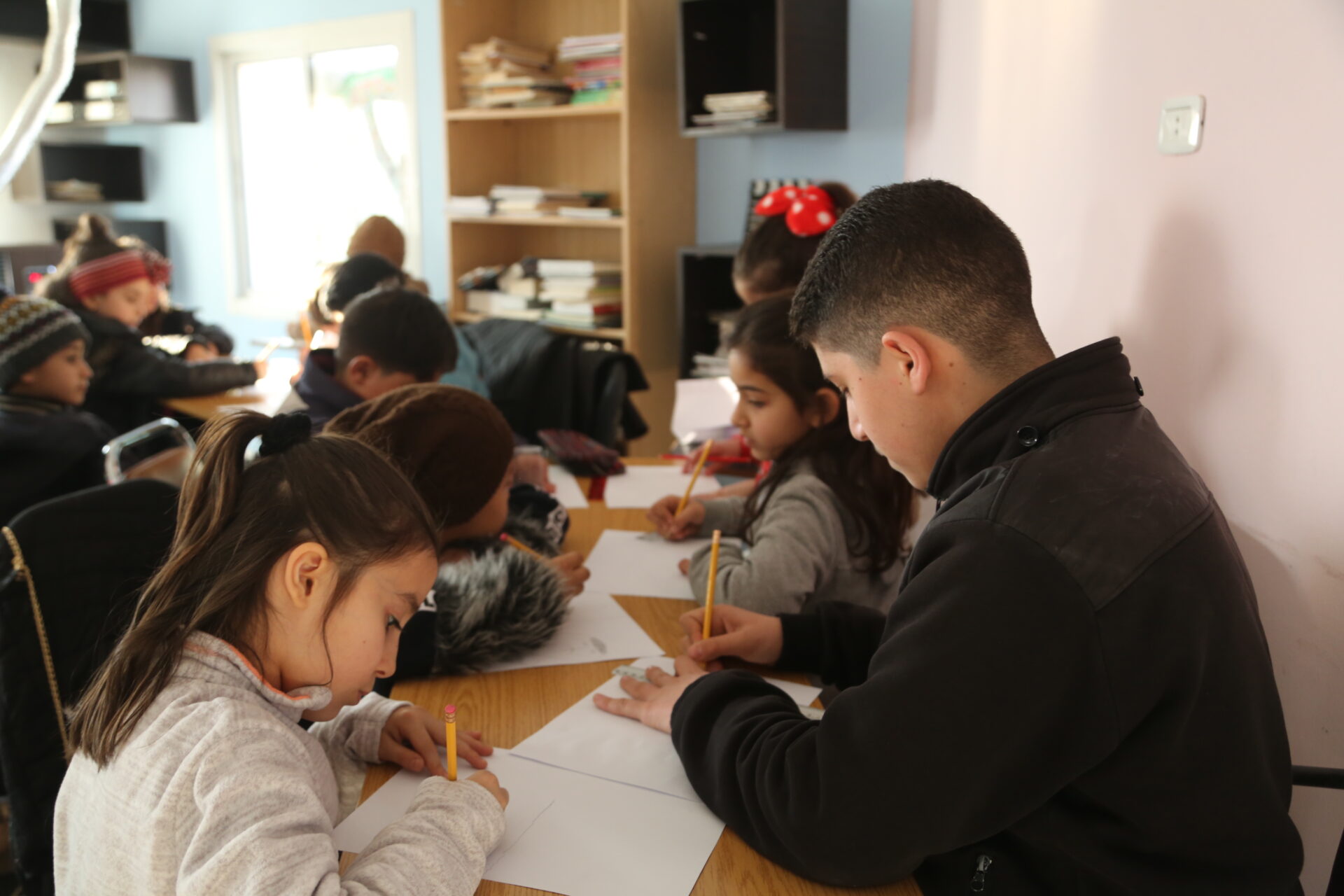 Students writing on sheets of paper while sitting together at a table.
