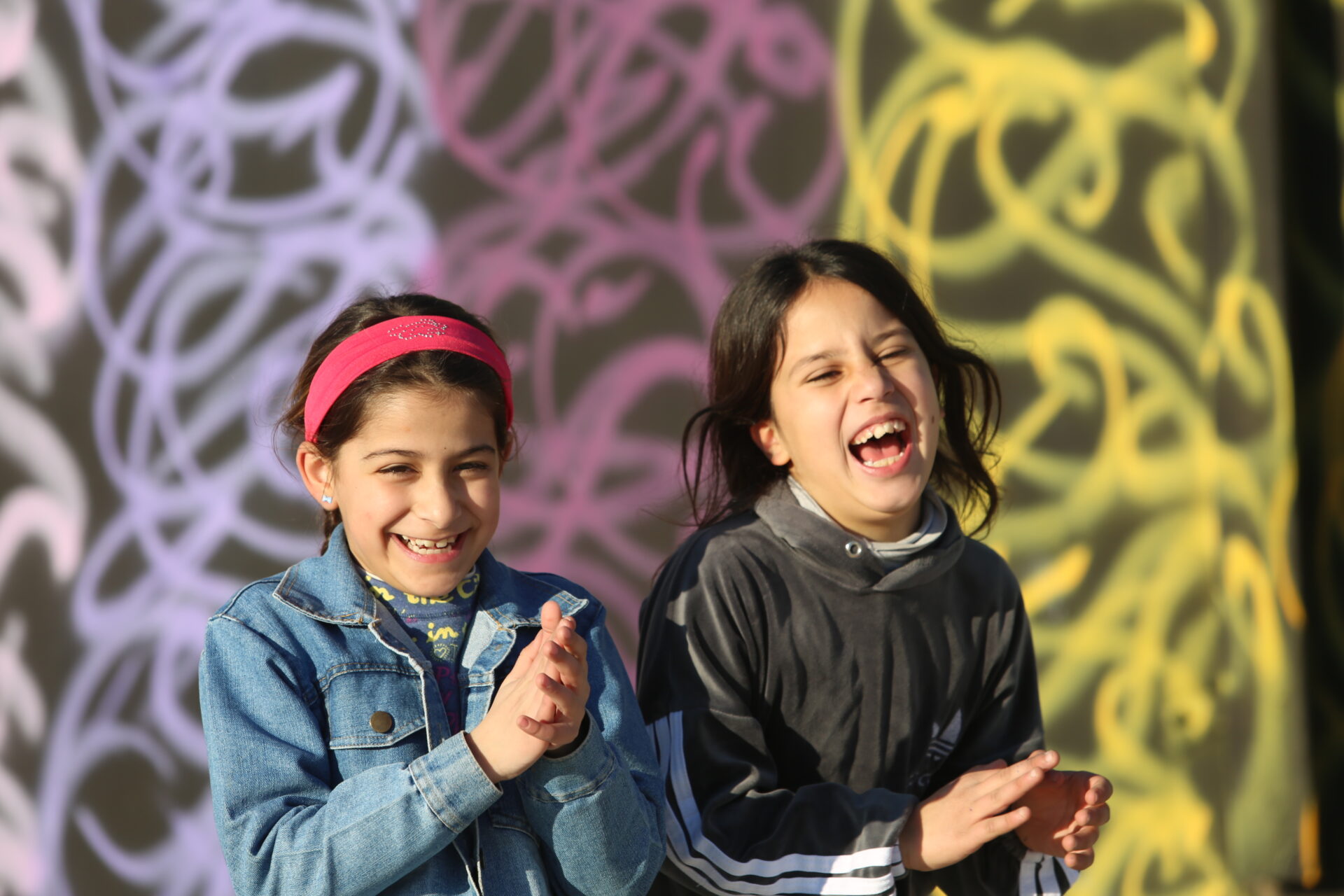 Two young girls looking ahead while laughing and clapping.