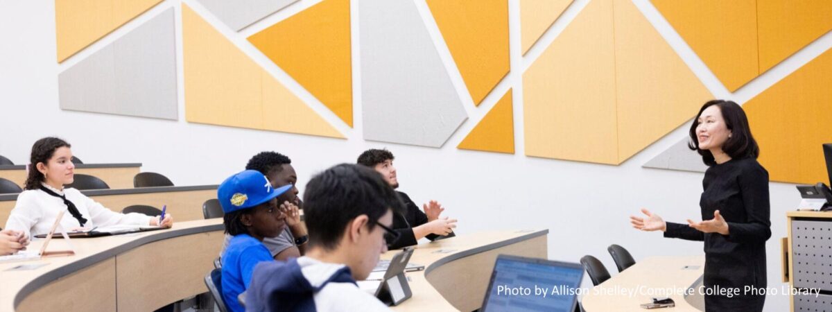 Multiethnic group of students listening to instructor in a large classroom on a college campus.