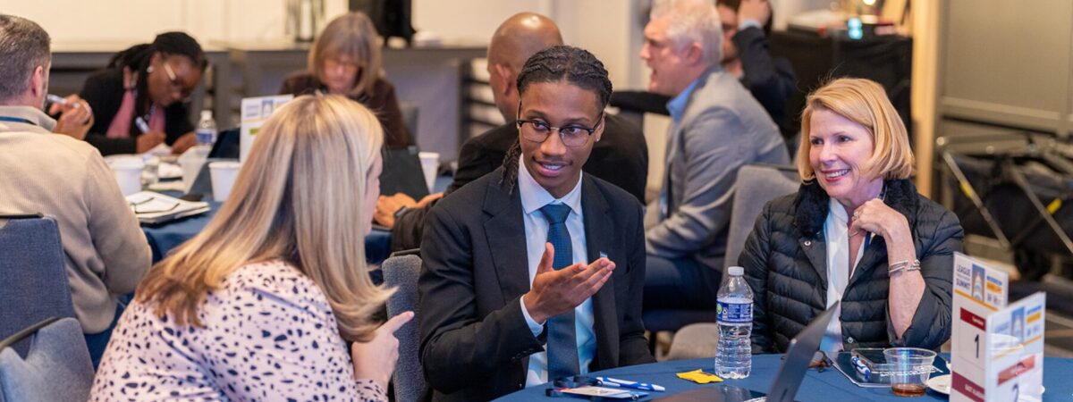 An image of student Seth Walker in a suit speaking with two district leaders at the League's 2025 Policy to Action Summit in Washington, DC.