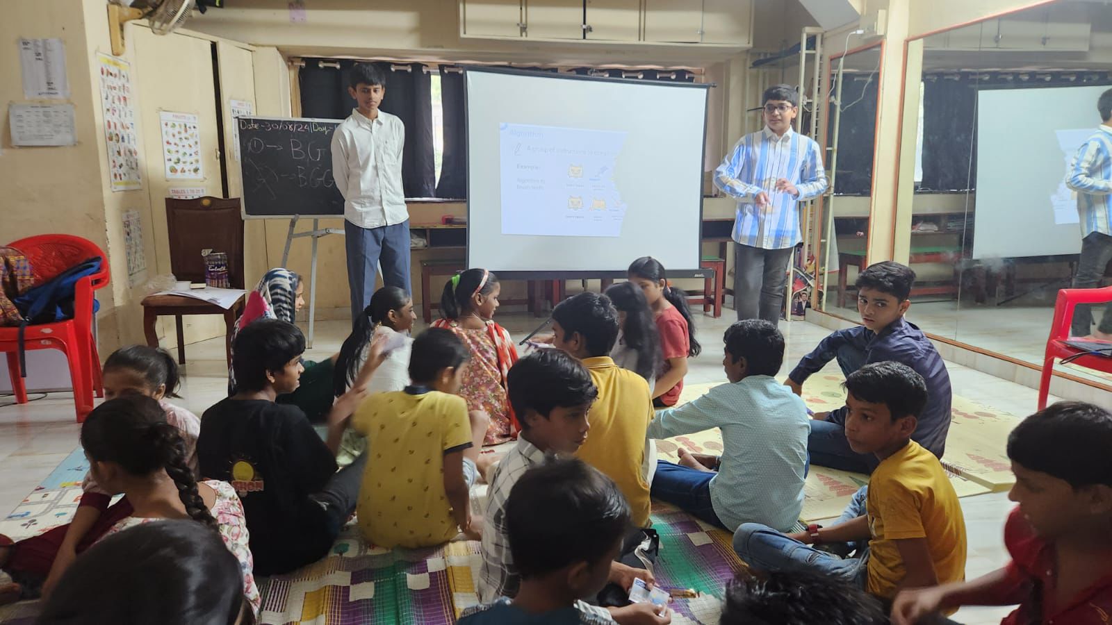 Two boys present to a classroom of younger students sitting on the floor
