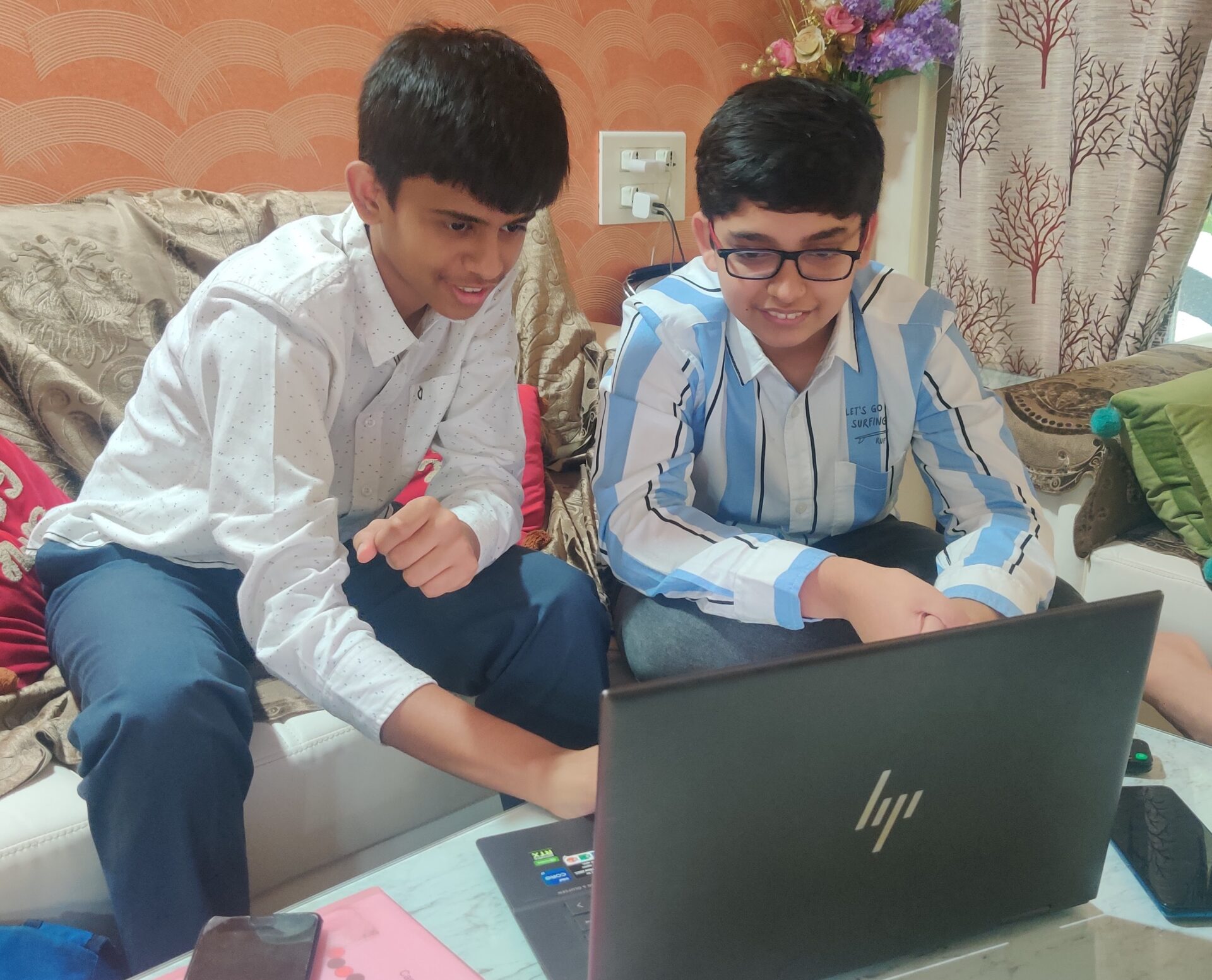 Two boys huddle around a laptop while seated on a couch