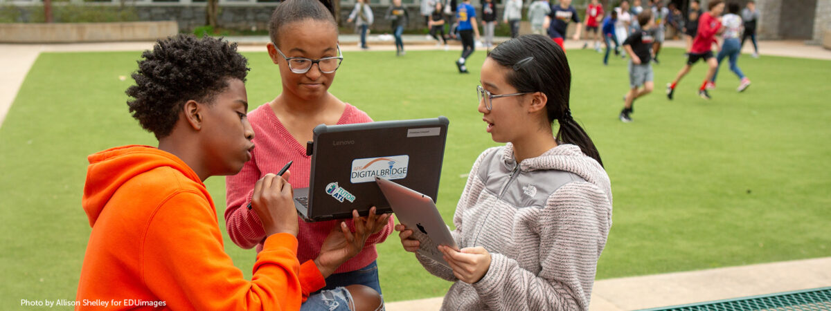 Three eighth-grade students work together on an assignment in a school courtyard.