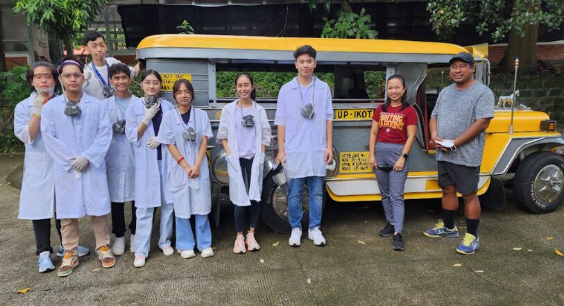 Students pose with community members in front of a yellow Philippine jeepney.