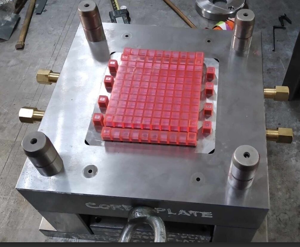 Early-stage prototype of recycled plastic math manipulatives arranged in a grid within a metal injection molding tool.