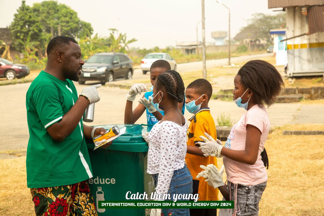 An adult and a group of young people gather around a recycling bin