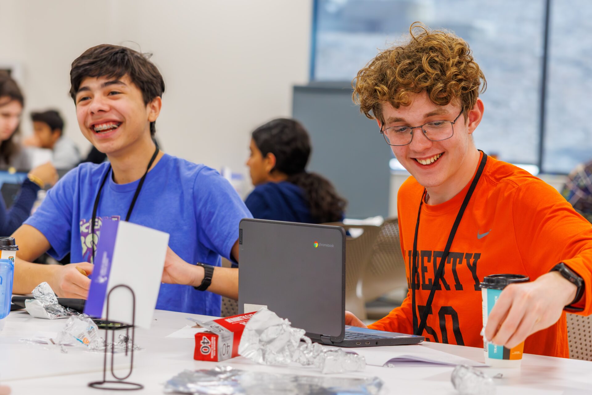 Two students seated at a table with laptops in front of them smile.
