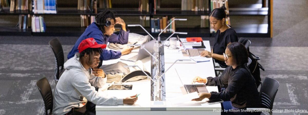 Group of Black students studying individually at a table at a college library.