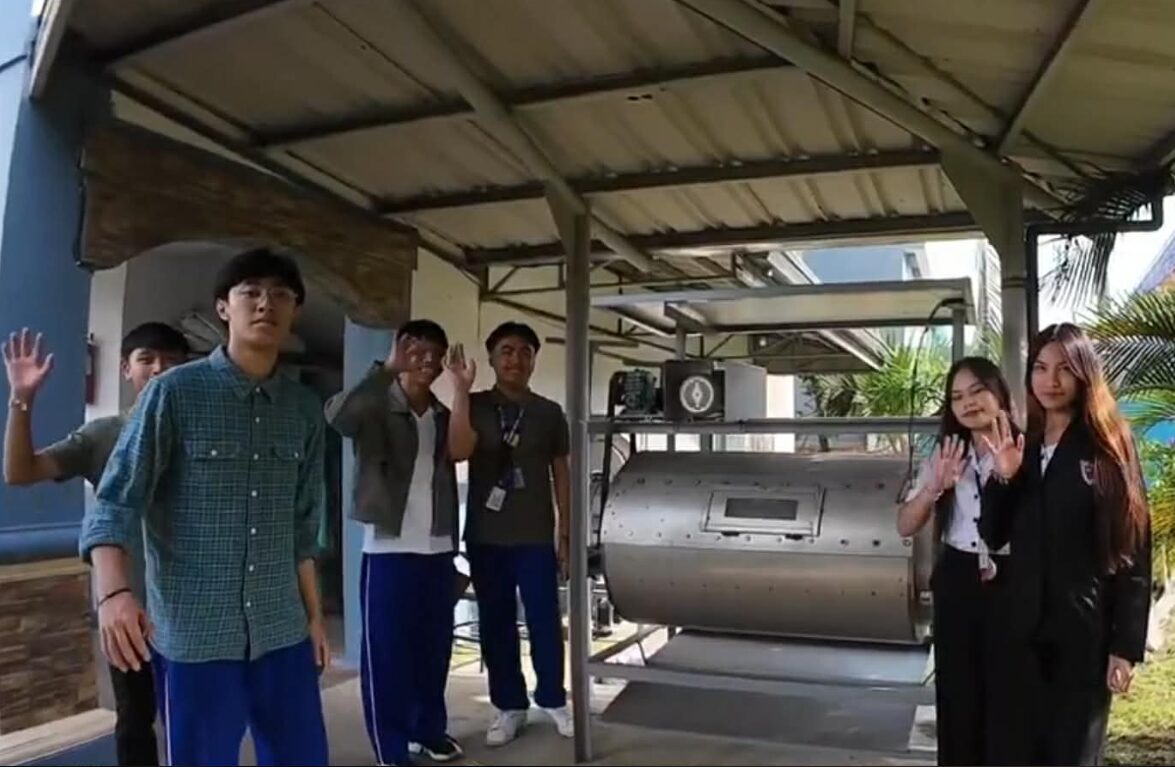 A group of students pose next to a large, cylindrical tank. 