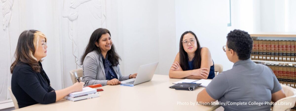 Asian and Black female faculty meeting around a table in a meeting room on a college campus.